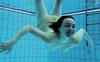 Brunette lady takes off her swimsuit while swimming underwater